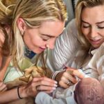 Vanessa Kirby smiling with loved one, joyfully holding her newborn baby in hospital bed.